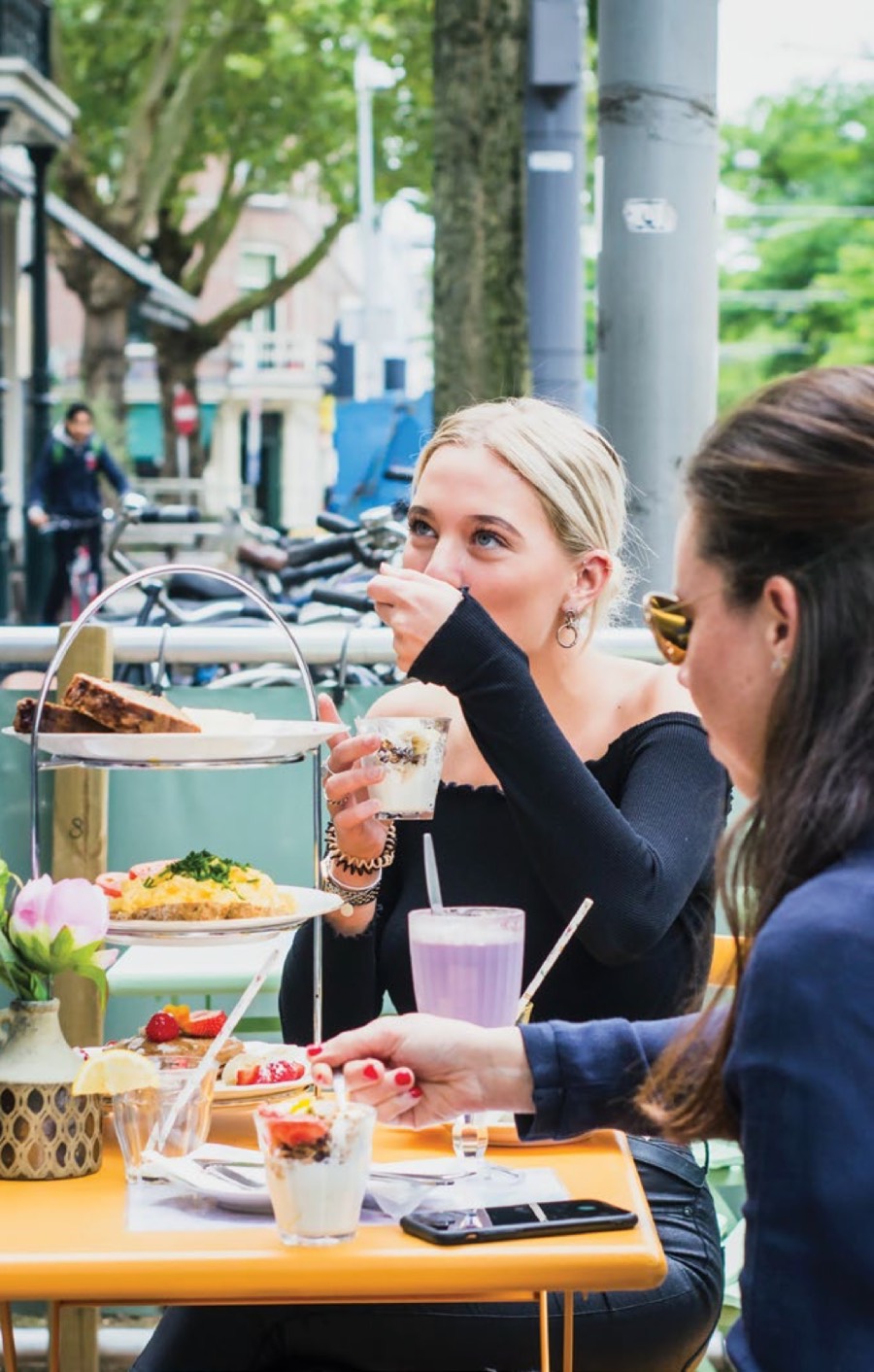 Two friends sharing pastries and drinks at a sunny patio table